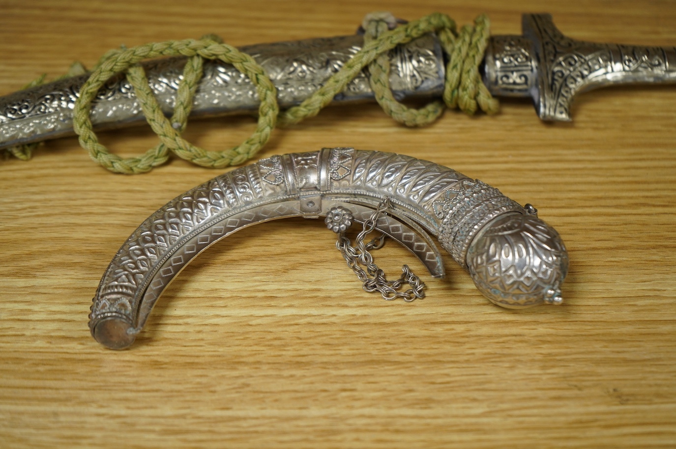 An Omani silver spice box in the form of a curved powder flask, together with a Moroccan dagger Jambiya with nickel hilt and sheath, both 20th century. Condition - fair.